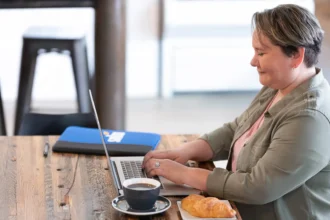 A female healthcare professional at her desk at night, studying on a laptop, demonstrating the flexibility of an online master's in healthcare administration